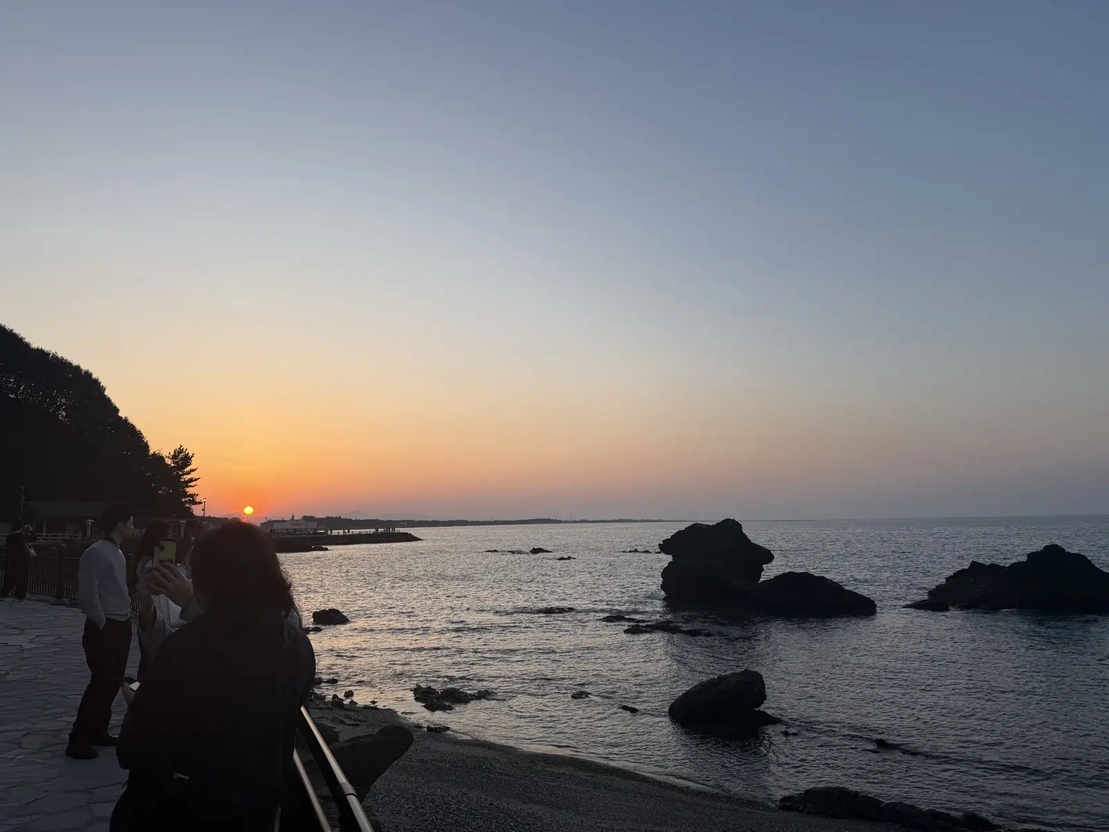 Sunset over the sea at Futami near Ise, with the horizon glowing orange, rocks in the water and people watching from the shore