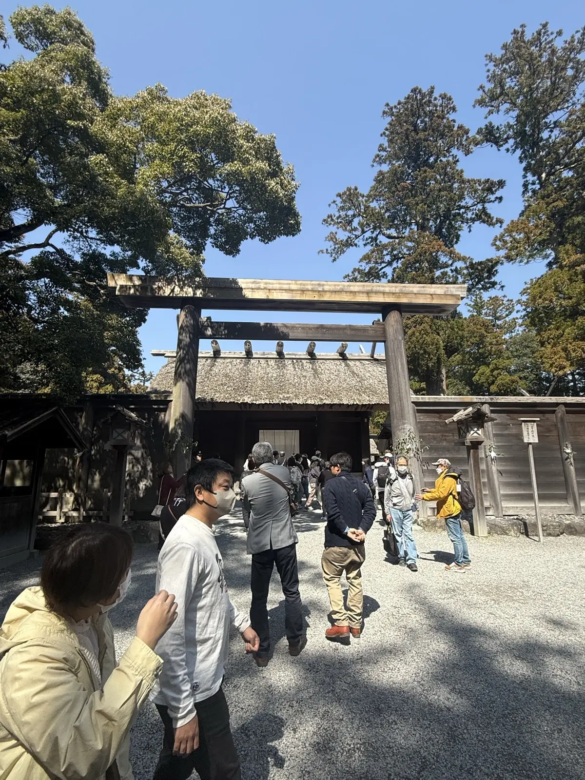 A plain wooden gate with a white cloth and thatched roof at Ise Jingu, the point beyond which photography is not allowed, with visitors approaching