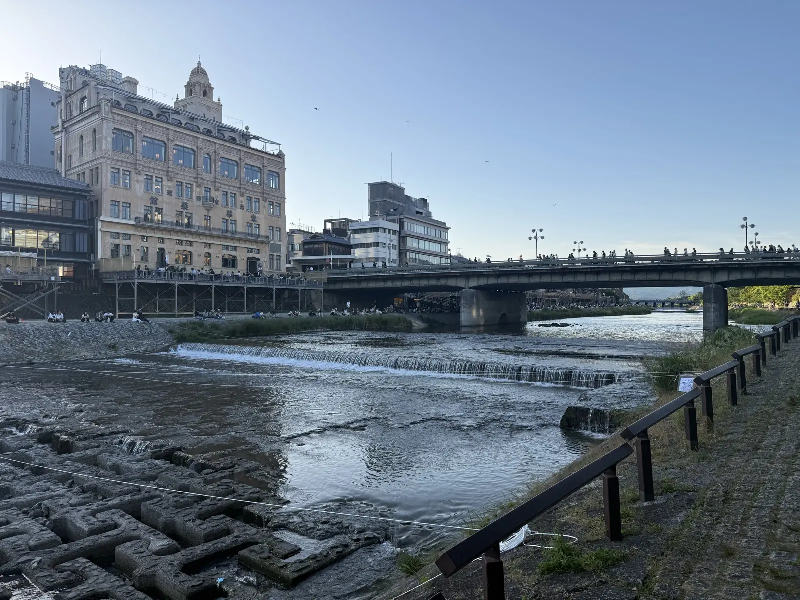 The Kamo river in central Kyoto with stepping-weirs, a bridge and riverside buildings — our own photo