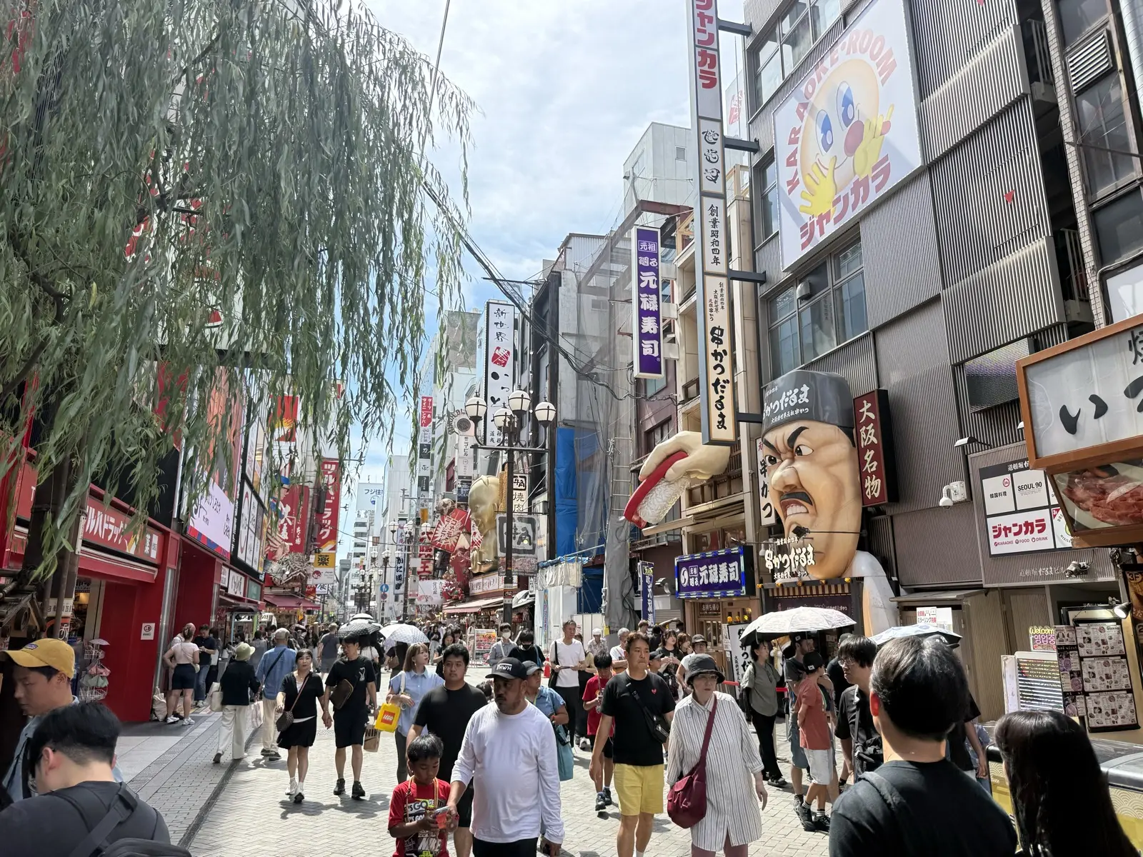 The Kushikatsu Daruma signboard in Osaka, featuring its famous angry-chef mascot face, above a crowded street