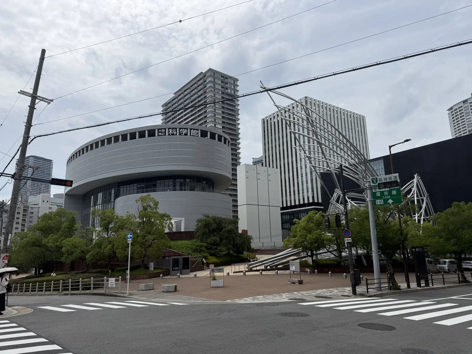 The round silver Osaka Science Museum with its 科学館 sign on the left, and the silver steel-tube sculpture marking the underground National Museum of Art (NMAO) entrance on the right