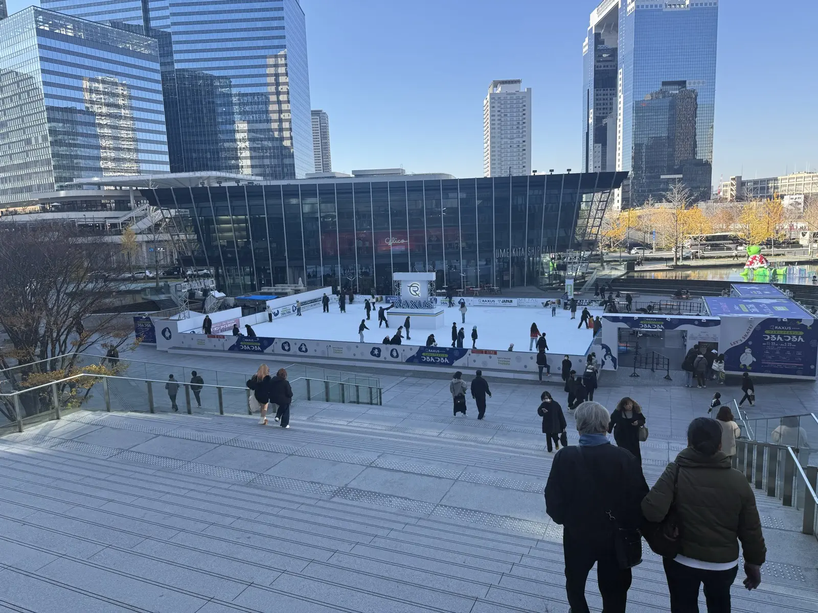 An open-air winter ice-skating rink in the Umekita plaza in front of Osaka Station, framed by skyscrapers on a clear day
