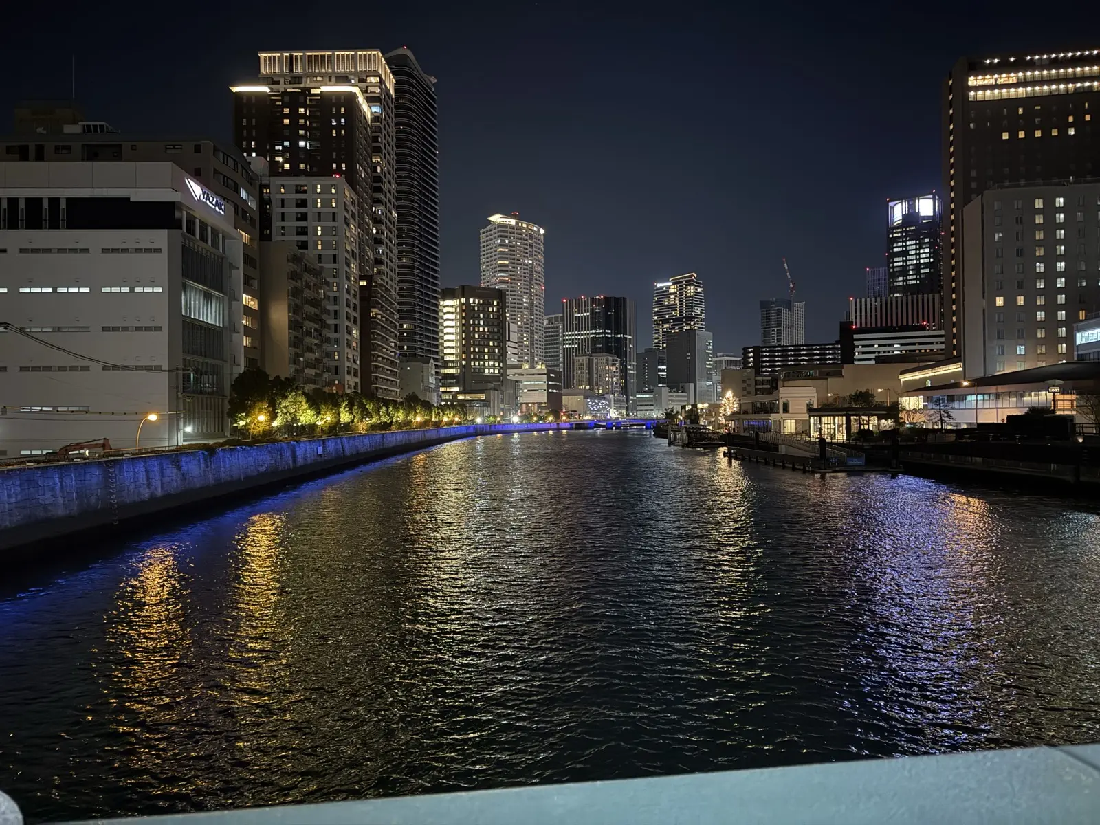 The river at Nakanoshima at night, skyscrapers and a blue-lit bridge reflected in the calm water