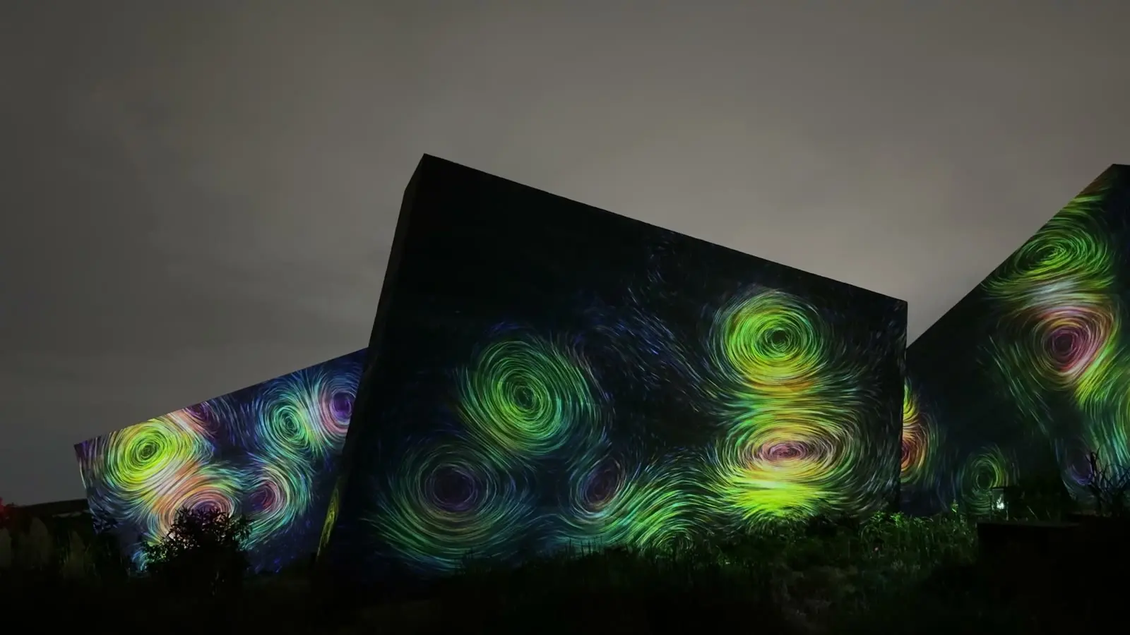 Swirling Van Gogh-like green and blue patterns projected onto angular walls in the garden at night