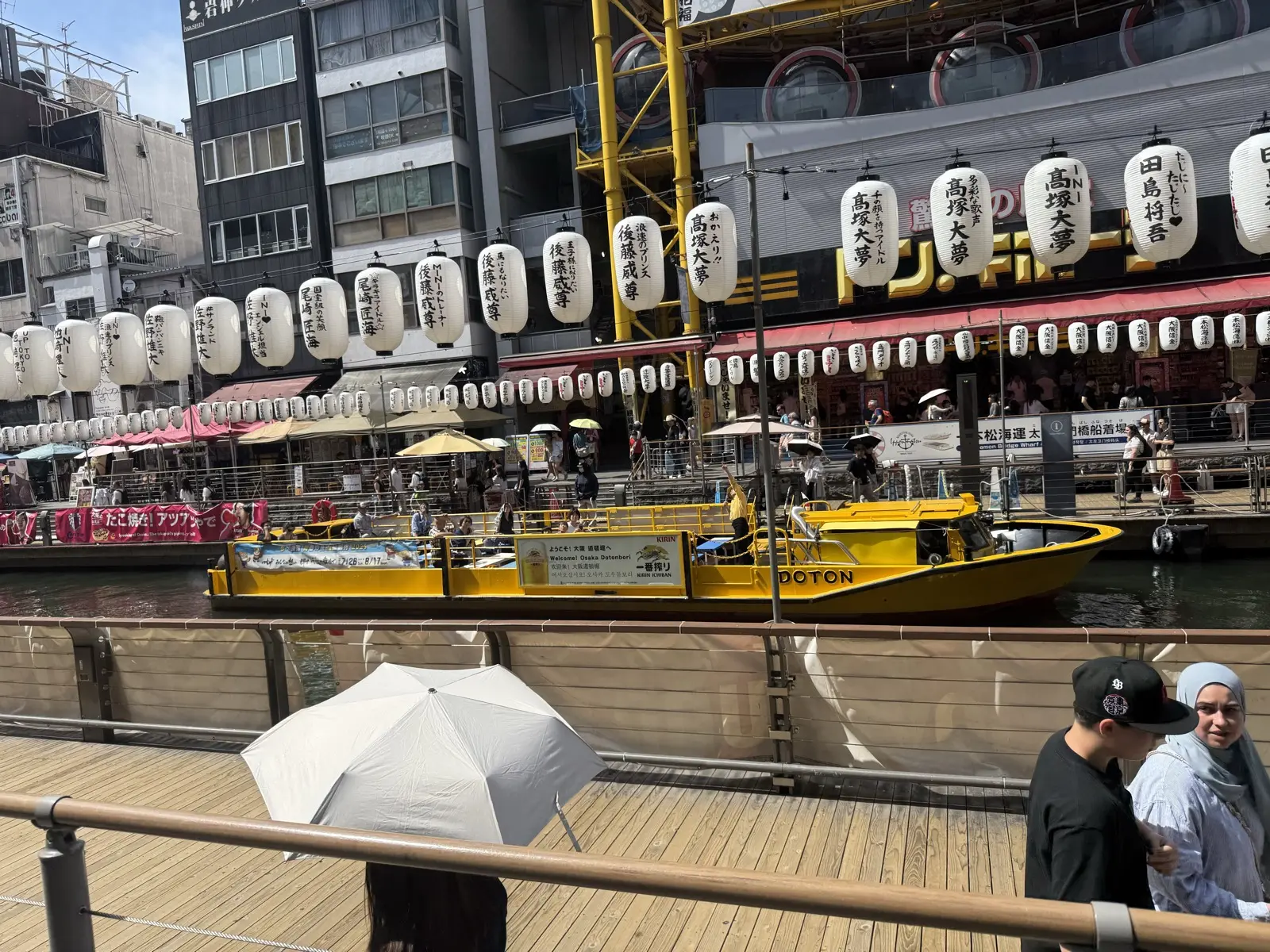 The yellow Tombori River Cruise boat on the Dotonbori canal, with rows of white paper lanterns lining the riverwalk