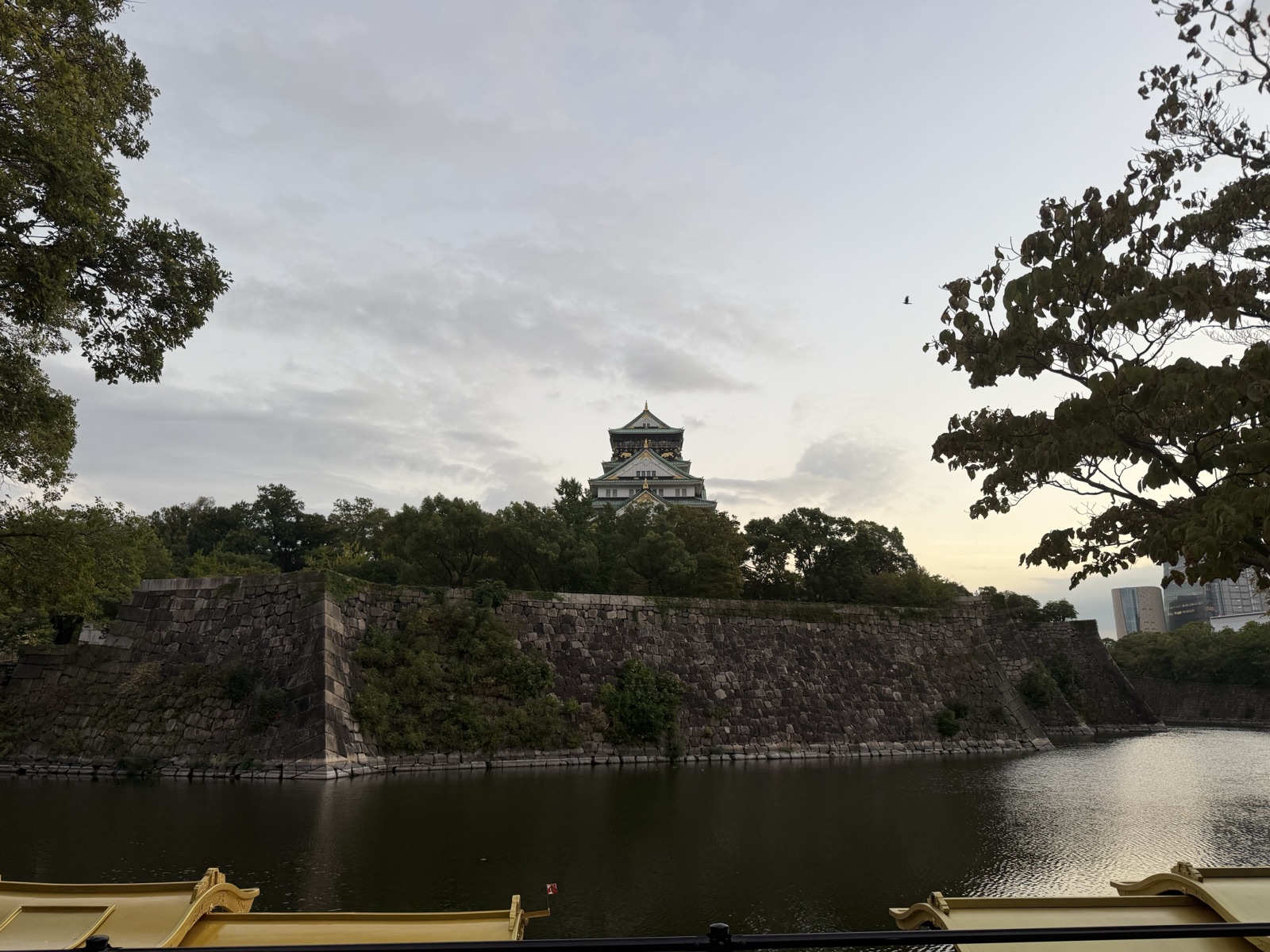 Osaka Castle main tower across the inner moat and stone walls at dusk, with a boat in the foreground